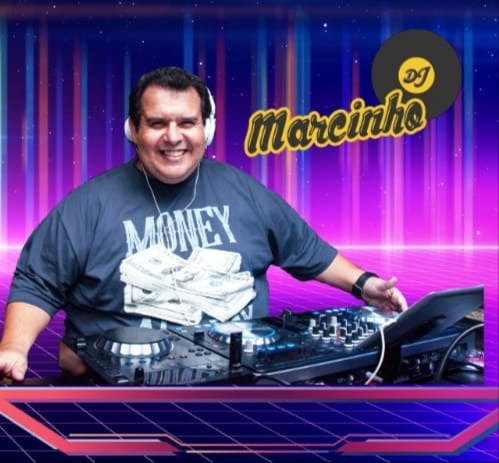 Marcinho DJ sorrindo em sua mesa de mixagem